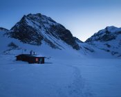 Кабіна в снігу біля гори на заході сонця — стокове фото