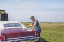 Зріла жінка подорожує на старовинній машині, дивлячись на карту на полі — стокове фото