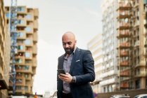 Visão de baixo ângulo de homem de negócios barbudo sorridente usando smartphone na cidade — Fotografia de Stock