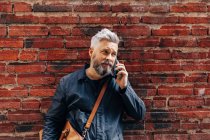Uomo accanto muro di mattoni parlando su smart phone — Foto stock