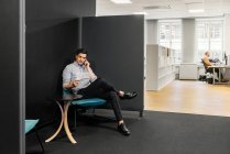Молодой человек сидит и разговаривает по телефону в офисе — стоковое фото