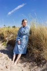 Teenage girl in bathrobe by grass on beach dune — Photo de stock