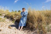 Teenage girl in bathrobe by grass on beach dune — Stock Photo