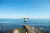 Young man standing on rock by sea — Photo de stock