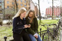 Mujeres jóvenes usando teléfono inteligente en el parque en Estocolmo, Suecia - foto de stock