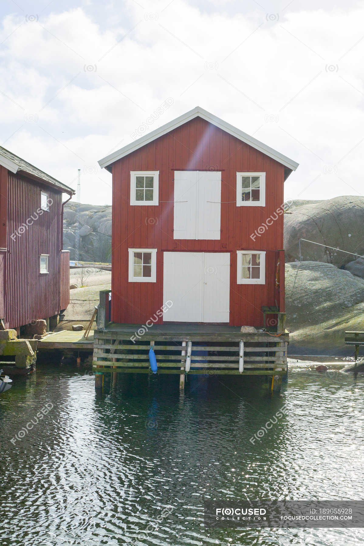 Red houses by water against sky with clouds — vertical, sunlight ...