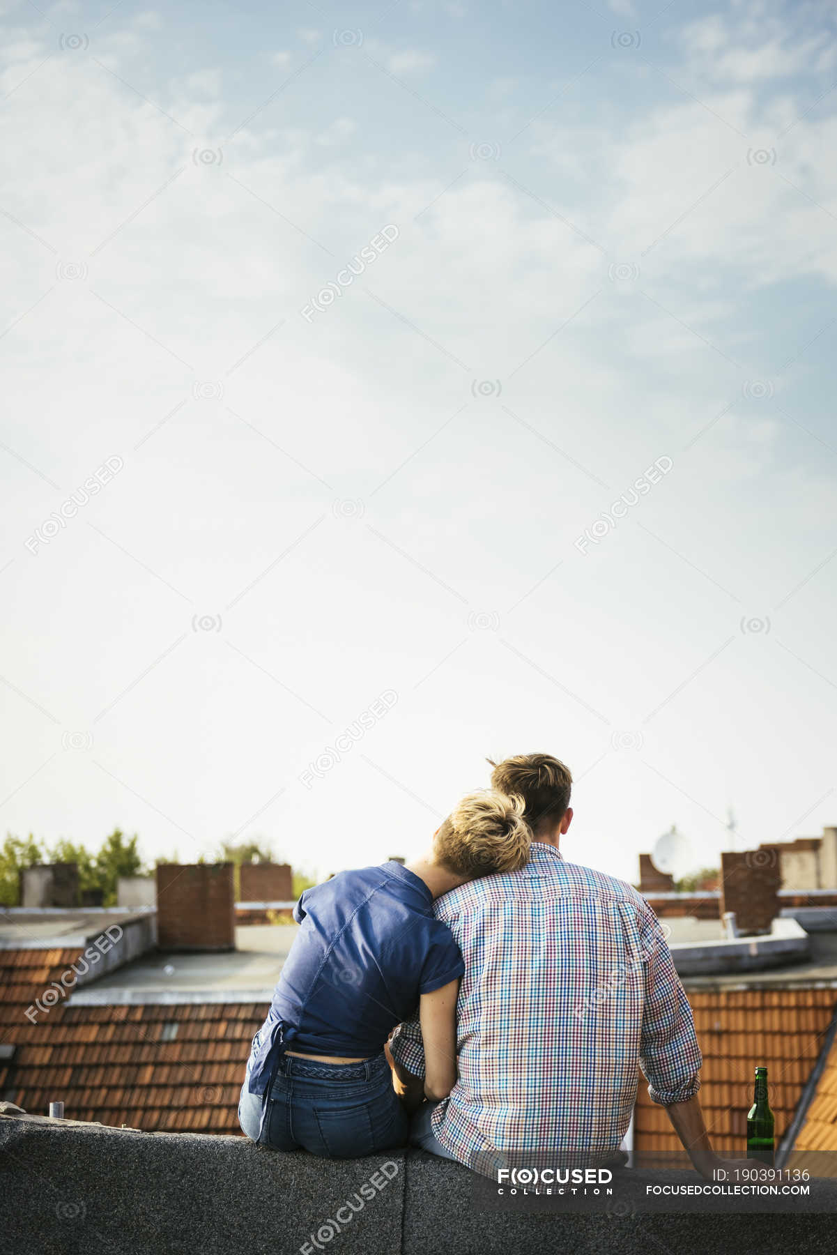 Rear view of young couple sitting on rooftop together — roofing, sky