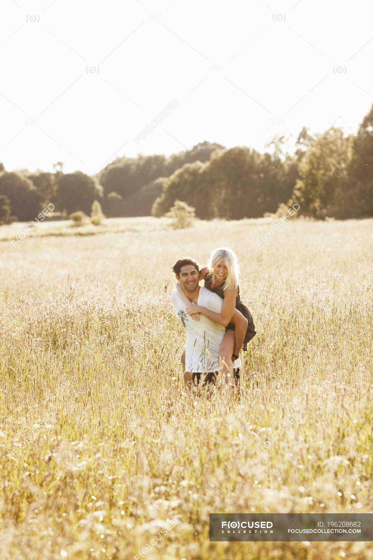 Young Couple Riding Piggyback In Meadow Outdoors Smiling Stock Photo 196208682