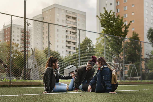 Les adolescentes utilisant un téléphone intelligent et assis ensemble sur un court de tennis — Photo de stock