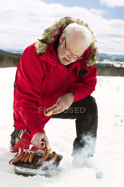 Homme cuisinant des hot-dogs dans la neige, se concentrer sur l'avant-plan — Photo de stock