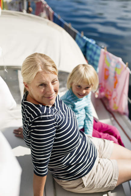 Madre e hija sentadas en la cubierta del barco y mirando a la cámara - foto de stock