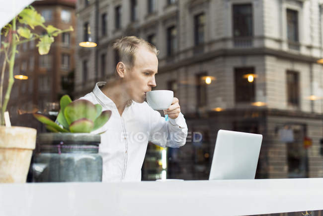 Чоловік в білій сорочці п'є чай і дивиться на ноутбук — стокове фото