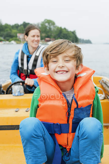 Portrait of boy on motor boat, mother in background — Stock Photo