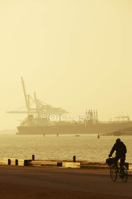 Чоловік їде на велосипеді в порту, корабель на задньому плані — стокове фото