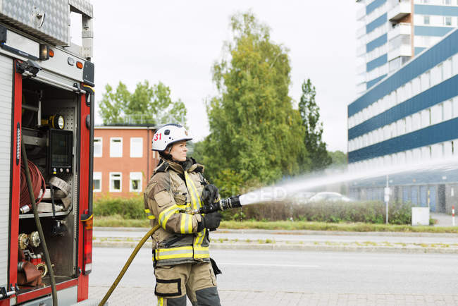 Female firefighter using fire hose next to truck — Stock Photo
