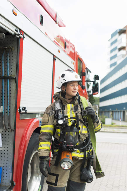 Bombeiro fêmea com equipamento em pé ao lado do caminhão de bombeiros — Fotografia de Stock