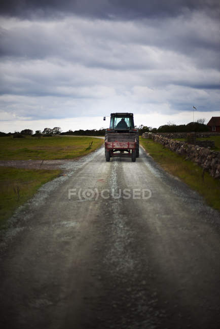 Трактор движется по сельской дороге под облачным небом — стоковое фото