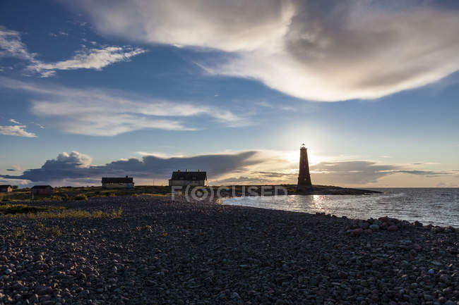 Nuages au-dessus du littoral et silhouette du phare en contre-jour — Photo de stock