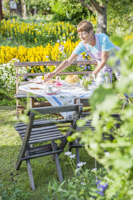 Mulher que põe a mesa no jardim iluminado sol — Fotografia de Stock