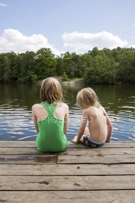 Rear view of children sitting on wooden jetty — Stock Photo