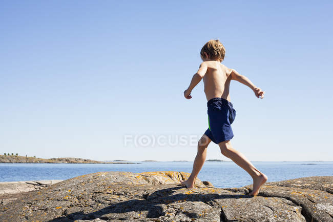 Мальчик бежит босиком по скалам у моря — стоковое фото
