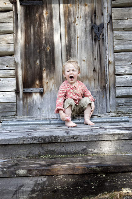 Boy with blonde hair sitting in front of cottage — Stock Photo