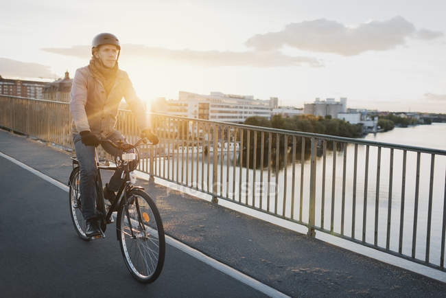 Homem andar de bicicleta na ponte ao pôr do sol, foco seletivo — Fotografia de Stock