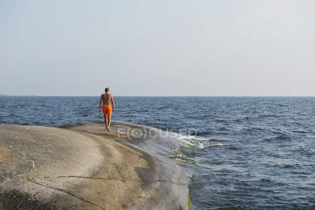 Vista trasera del hombre caminando a lo largo del mar - foto de stock