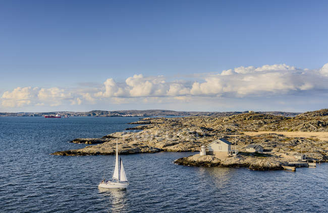 Vista de la costa y velero en el agua en la luz del sol brillante - foto de stock