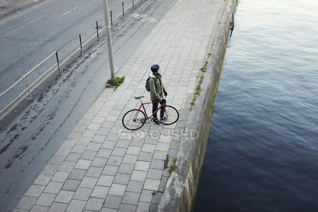 Homem com bicicleta em pé na margem do rio, foco seletivo — Fotografia de Stock