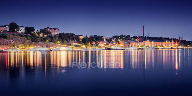 Coastal buildings illuminated at night reflecting in water — Stock Photo