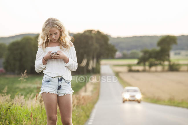 Дівчина-підліток з мобільним телефоном, що стоїть на узбіччі дороги — стокове фото
