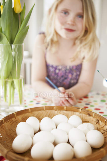 Ragazza seduta al tavolo con cesto di uova, focus selettivo — Foto stock