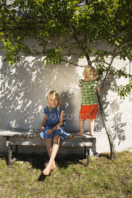 Hermana con hermano en patio trasero banco en verano - foto de stock