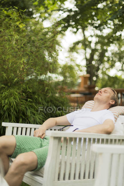 Hombre relajante con los ojos cerrados en silla en el patio trasero - foto de stock