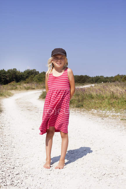 Chica en vestido rosa de pie en el camino de tierra - foto de stock