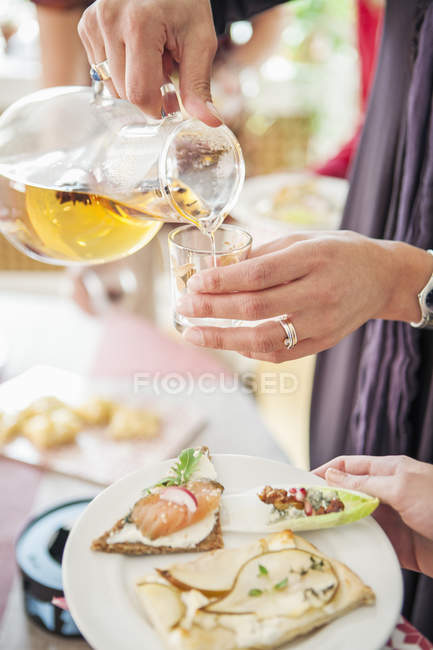 Female hands pouring ice tea from jug to glass and other holding plate — Stock Photo