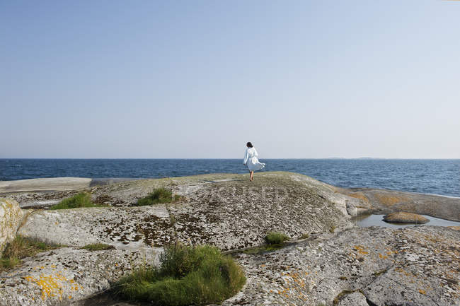 Vue arrière de la fille sur le rocher regardant la mer — Photo de stock