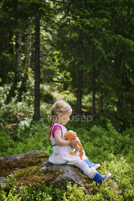Vue latérale de la fille assise avec poupée sur le rocher — Photo de stock