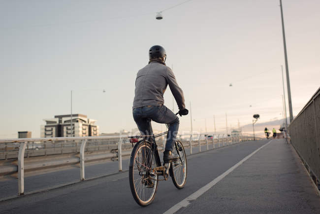 Vue arrière de l'homme en vélo sur le pont au coucher du soleil — Photo de stock