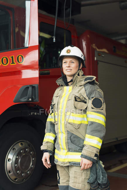 Female firefighter in uniform standing by fire engine — Stock Photo