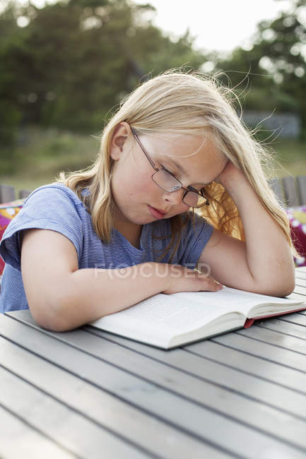 Menina livro de leitura à mesa ao ar livre, foco diferencial — Fotografia de Stock