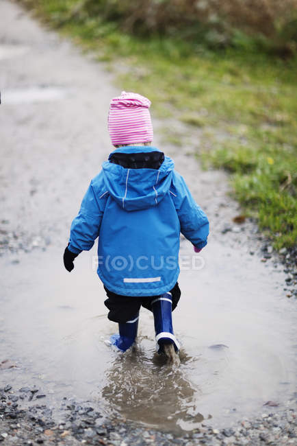 Vue arrière de la fille marchant à travers la flaque d'eau — Photo de stock