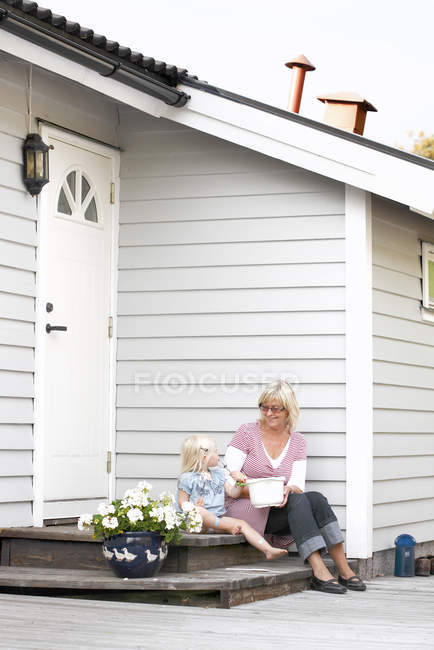 Donna anziana seduta con ragazza sul portico — Foto stock