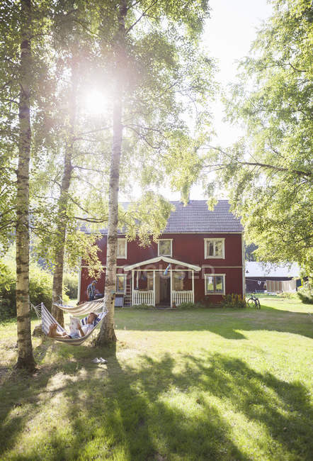 View of man lying in hammock, cottage house in sunlight — Stock Photo