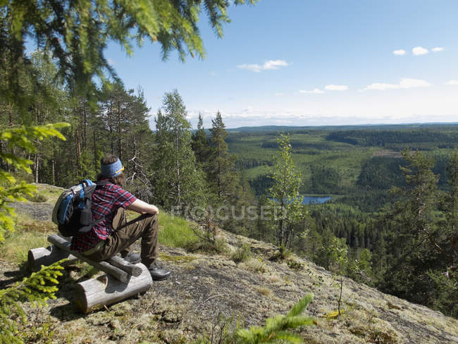 Hiker sitting on wooden bench in forest and looking at view — Stock Photo