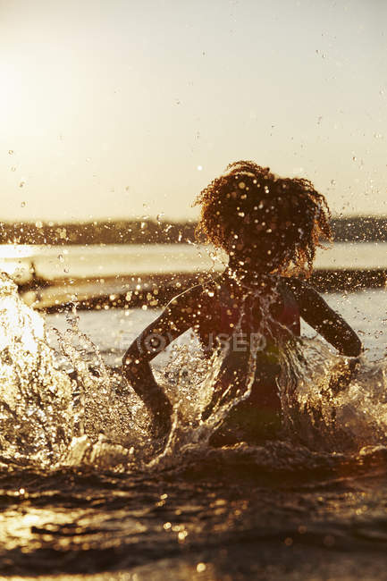 Vue de face de fille éclaboussures dans le lac au coucher du soleil — Photo de stock