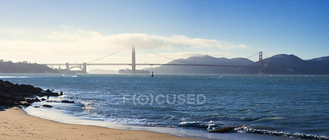 Scenic view of beach with suspension bridge in background — Stock Photo