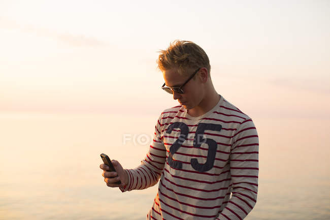 Man in glasses using smartphone by lake, focus on foreground — Stock Photo