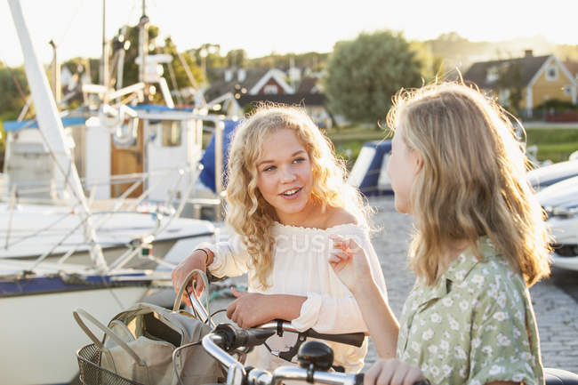 Two teenage girls with bicycles talking at marina bay — Stock Photo